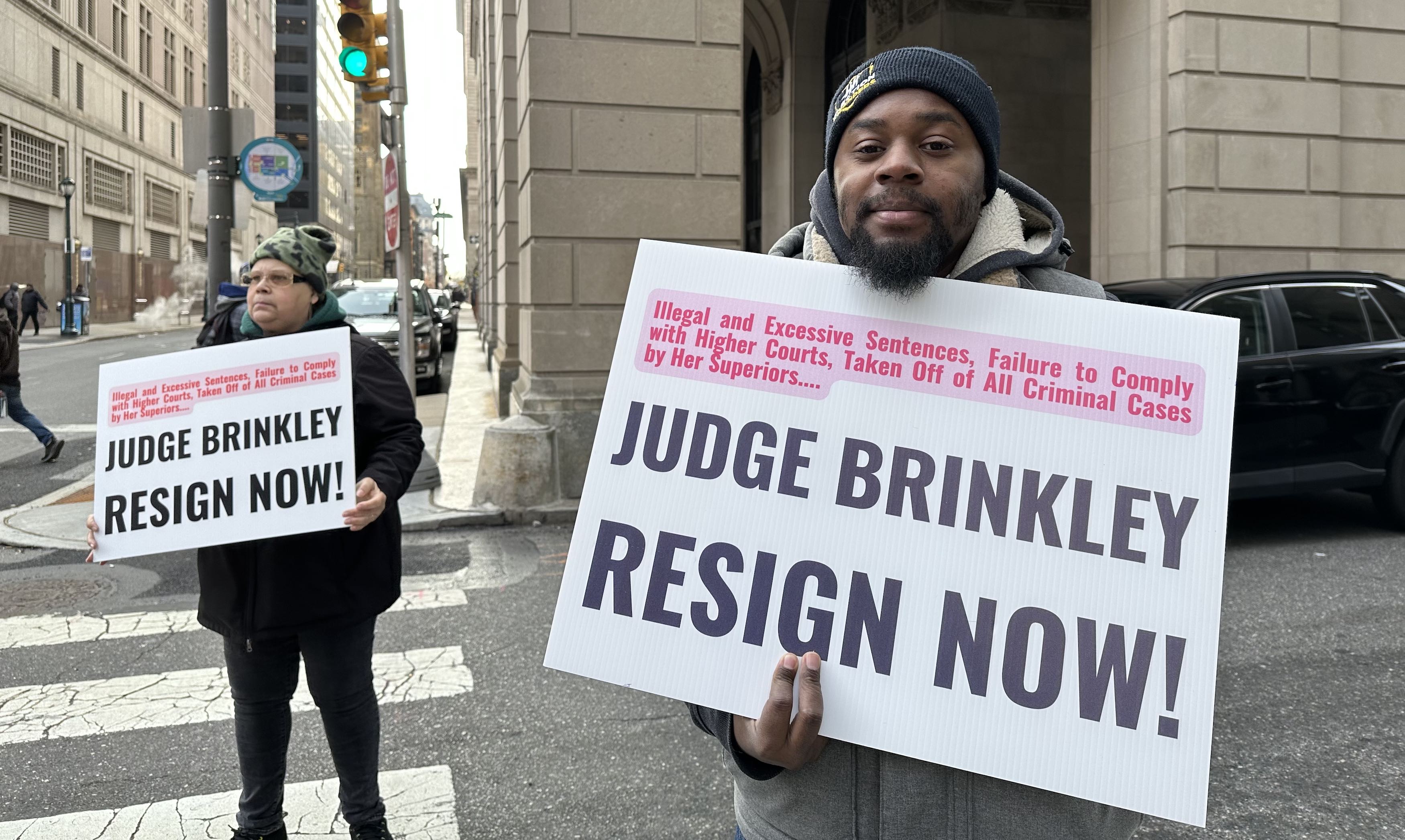 Derrick from Amistad Movement Power and Mrs Dee Dee hold signs demanding Judge Brinkley's resignation