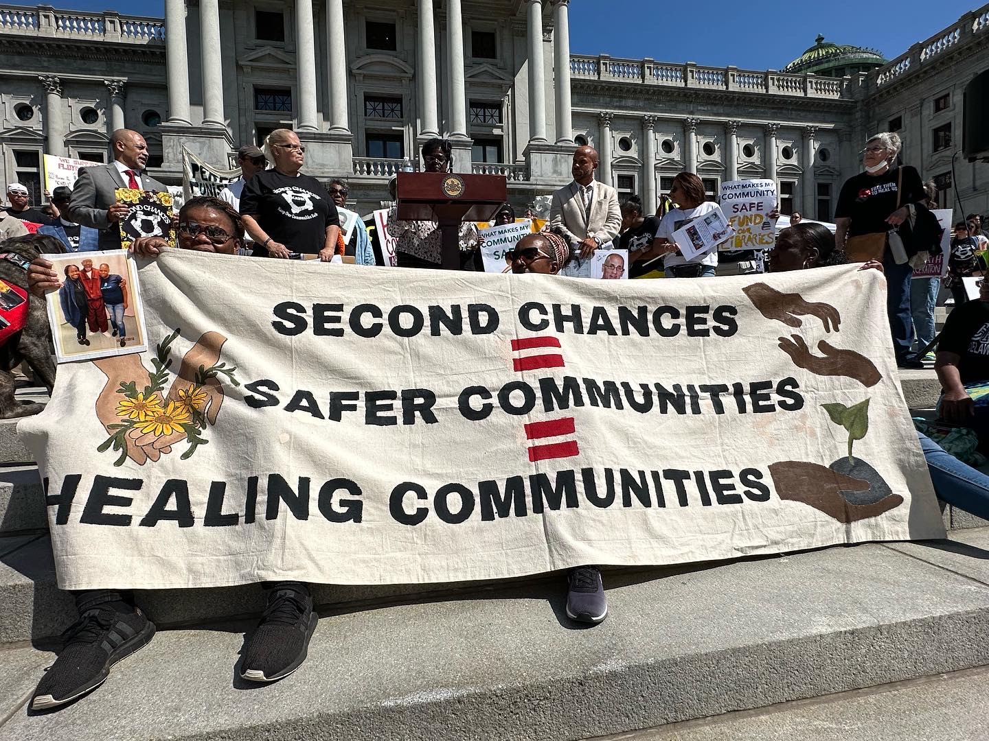 A group of people hold signs and banners at Coalition to Abolish Death By Incarcerations annual rally