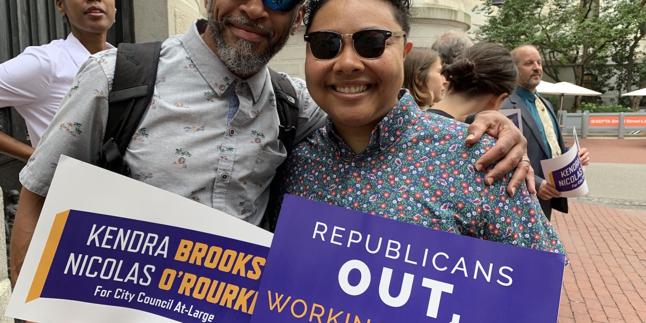 Kris Henderson and Kempis Songster hold signs that read 'Republicans Out, Working Families In' and 'Kendra Brooks and Nicolas O'Rourke