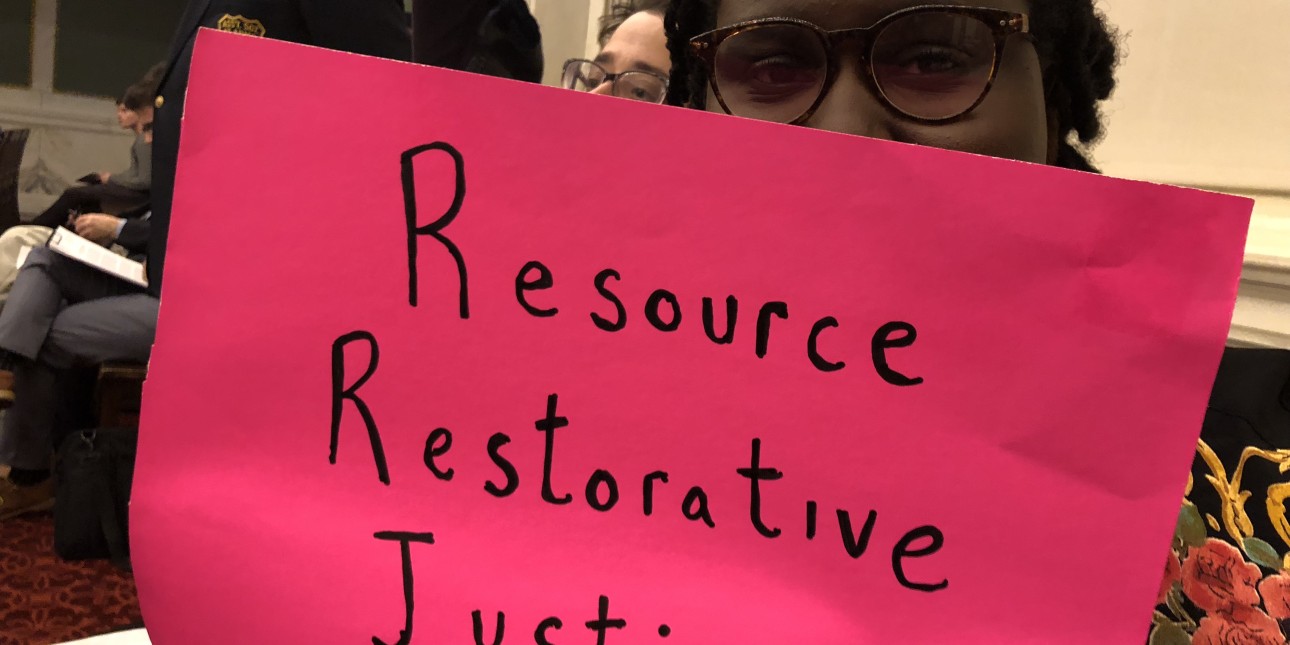 Nikki Grant holds a sing that reads 'Resource Restorative Justice'