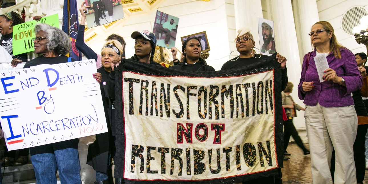 three women hold a banner that reads 'transformation not retribution next to sever other women including one holding a sign that reads 'end death by incarceartion'