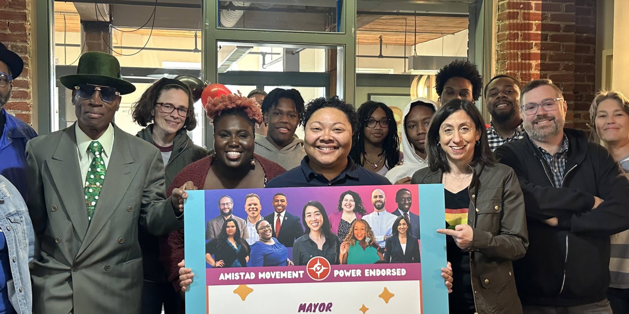 a group of people gathers together for a photo at Amistad Movement Power's volunteer celebration and holds a poster of endorsed candidates