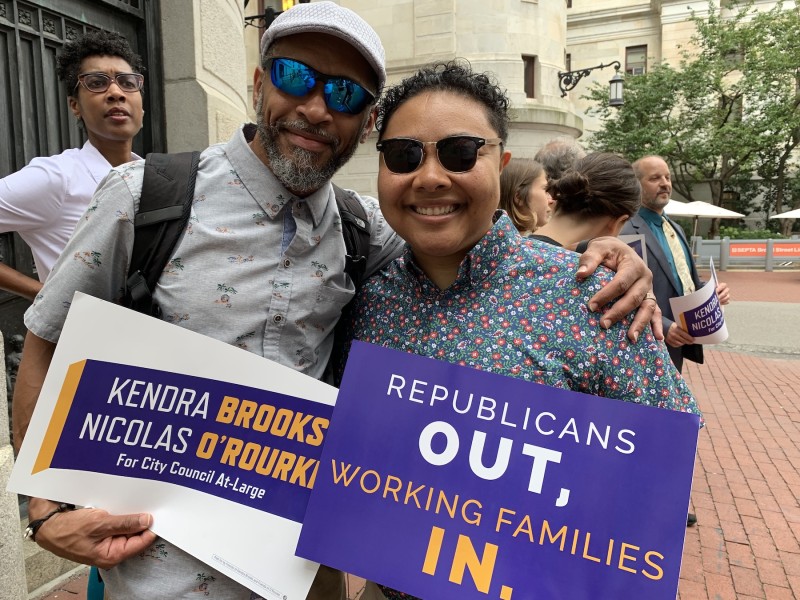Kris Henderson and Kempis Songster hold signs that read 'Republicans Out, Working Families In' and 'Kendra Brooks and Nicolas O'Rourke