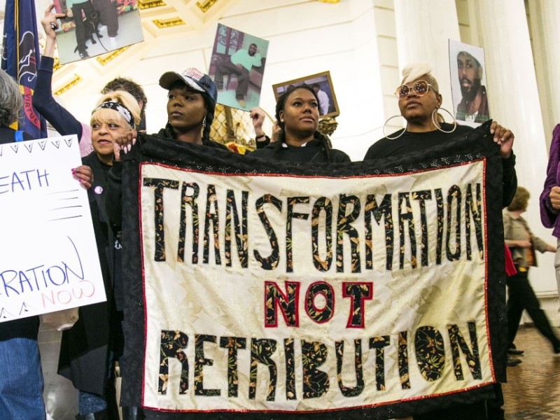 an image shows women holding a banner that says 'Transformation Not Retribution"